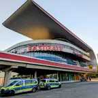 Modernes Einkaufszentrum mit geschwungener Dachkonstruktion und roter Aufschrift 'EASTGATE' sowie zwei geparkten Polizeifahrzeugen davor.