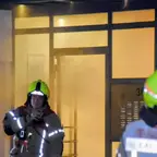 Zwei Feuerwehrleute mit gelben Helmen vor einem Hauseingang, aus dem Rauch dringt