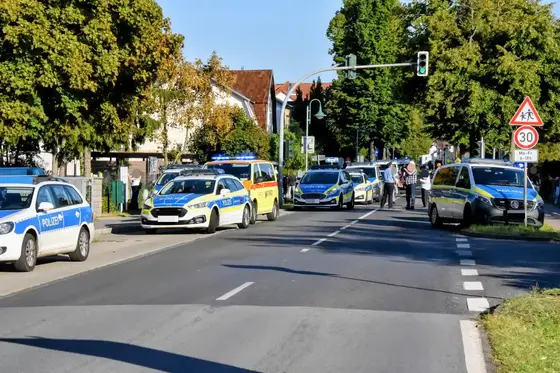 Mehrere Polizeifahrzeuge stehen an einer Straße in einer Wohngegend bei grünem Ampelsignal, zwei Personen stehen auf dem Gehweg