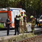 Mehrere Feuerwehrleute und Polizisten stehen auf einer Straße neben einem Feuerwehrfahrzeug und einer Straßenbahn