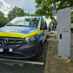 Polizeiwagen steht neben einer Ladesäule auf einem Parkplatz an einem Baum gesäumten Straßenrand. An der Ladesäule befindet sich Blut.