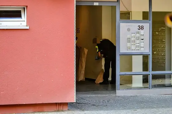 Polizistin sichert Beweise im Hauseingang eines Wohngebäudes mit roter Fassade und grauem Türrahmen