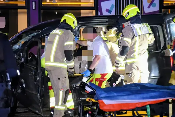 Mehrere Einsatzkräfte in Schutzkleidung und Helm retten einer eingeklemmte Person aus einem beschädigten Fahrzeug, daneben eine leere Trage.