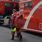 Person in rotem Schutzanzug mit gelbem Helm in der Hand geht an einem roten Fahrzeug mit der Aufschrift 'CBRN' vorbei