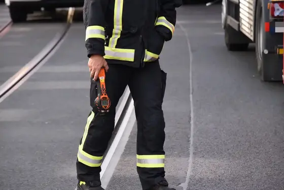 Feuerwehrmann in Schutzkleidung hält ein orangefarbenes Messgerät für Chemie und Gase auf einer Straße mit weißen Fahrbahnmarkierungen.
