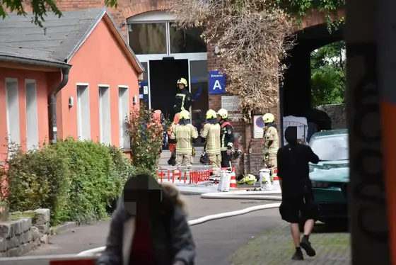 Einsatzkräfte in Vollschutzanzug an einem Dekontaminationsplatz vor einem Gebäude mit roter Fassade und einem Torbogen.