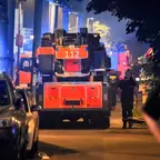 Feuerwehrfahrzeug mit der Nummer 112 steht nachts auf einer Straße, umgeben von parkenden Autos und mehreren Personen, darunter mehrere Personen in Polizeiuniform