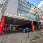 Einfahrt zu einem Gebäude mit rotem Rahmen und der Aufschrift 'Lagerabteile 1-50 m² zu mieten' über dem Eingang.