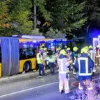 Mehrere Feuerwehrleute in Schutzkleidung stehen nachts neben einem gelben Gelenkbus und einem Einsatzfahrzeug mit Blaulicht auf einer Straße.
