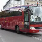 Roter Reisebus mit Mercedes-Stern auf einer Stadtstraße vor Ampelkreuzung.
