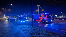 Rotes Feuerwehrfahrzeug mit Blaulicht steht im Dunkeln auf einer Straße, daneben und dahinter weitere Einsatzfahrzeuge.