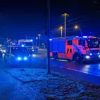 Rotes Feuerwehrfahrzeug mit Blaulicht steht im Dunkeln auf einer Straße, daneben und dahinter weitere Einsatzfahrzeuge.