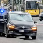 Schwarzer VW mit eingedrückter Frontscheibe steht an Unfallstelle, dahinter ein Polizeiauto mit Blaulicht und eine gelbe Straßenbahn.