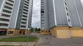 Zwei hohe Wohngebäude mit grauen Fassaden und weißen Balkonen, dazwischen eine abgesperrte Zufahrt mit rot-weißem Absperrband.