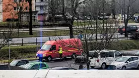 Rotes Einsatzfahrzeug mit Blaulicht steht auf Straße, daneben mehrere geparkte Autos und Bäume ohne Blätter.