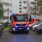 Zwei orange-rote Feuerwehrfahrzeuge mit Blaulicht stehen in einer Wohnsiedlung zwischen geparkten Autos.