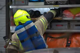 Feuerwehrmann mit gelbem Helm und Atemschutzgerät greift nach Ausrüstung in einem Fahrzeug.