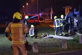 Feuerwehrleute in gelben Helmen und Schutzkleidung arbeiten in der Dunkelheit an einem umgekippten Kleinlaster an einer Wiese neben einer Straße.