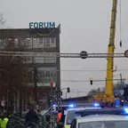 Straßenszene mit mehreren Einsatzfahrzeugen mit Blaulicht, einem gelben Kran und einem Gebäude mit dem Schriftzug 'FORUM Köpenick'.