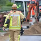 Mitarbeiter der Netzgesellschaft Berlin-Brandenburg, in gelber Schutzkleidung und Helm geht auf eine Baustelle mit Bagger und mehreren Einsatzkräften zu.