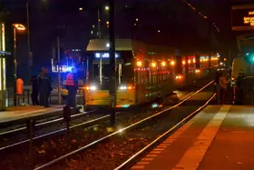 Nachtszene an einer Straßenbahnhaltestelle mit einer Straßenbahn der BVG, deren Warnblinkanlage eingeschaltet ist, und mehreren Mitarbeitern in Warnwesten auf dem Bahnsteig.