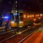 Nachtszene an einer Straßenbahnhaltestelle mit einer Straßenbahn der BVG, deren Warnblinkanlage eingeschaltet ist, und mehreren Mitarbeitern in Warnwesten auf dem Bahnsteig.