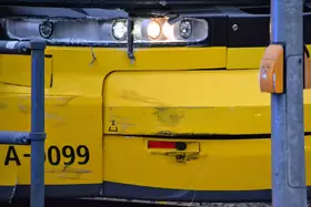 Nahaufnahme der vorderen linken Seite einer gelben Straßenbahn mit Kratzspuren und Delle, zwei Scheinwerfer leuchten.