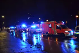 Mehrere Einsatzfahrzeuge mit Blaulicht stehen nachts auf einer nassen Straße in einer Reihe.