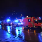 Mehrere Einsatzfahrzeuge mit Blaulicht stehen nachts auf einer nassen Straße in einer Reihe.