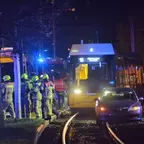 Auto steht auf Straßenbahngleisen, mehrere Feuerwehrleute in Schutzkleidung stehen daneben, Straßenbahn mit eingeschaltetem Licht im Hintergrund.