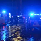 Mehrere Einsatzfahrzeuge mit eingeschalteten blauen Warnleuchten stehen nachts auf einer nassen Straße, Einsatzkräfte sind sichtbar.