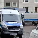 Mehrere weiße Polizeifahrzeuge mit blauen Streifen und Aufschrift "Polizei" sowie "Kriminaltechnik" vor einem mehrstöckigen Gebäude.