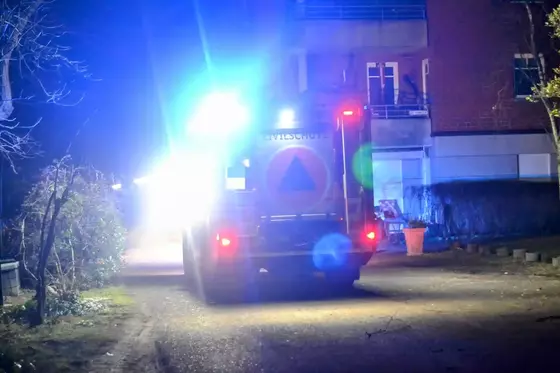 Rückansicht eines Einsatzfahrzeugs mit eingeschaltetem Blaulicht vor einem Wohngebäude in der Nacht.