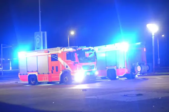 Zwei rote Feuerwehrfahrzeuge mit eingeschalteten blauen Warnlichtern bei Nacht auf einer Straße.