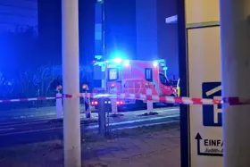 Rettungswagen mit eingeschaltetem Blaulicht steht nachts hinter Absperrband an einer Straße.