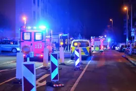 Mehrere Einsatzfahrzeuge mit Blaulicht stehen nachts auf einer Straße, davor Absperrungen mit reflektierenden Schildern.