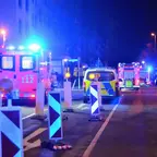 Mehrere Einsatzfahrzeuge mit Blaulicht stehen nachts auf einer Straße, davor Absperrungen mit reflektierenden Schildern.