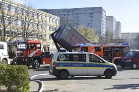 Polizeiwagen und Feuerwehrfahrzeuge vor einem Wohnhaus, Feuerwehrkipper hebt Container an.