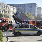 Polizeiwagen und Feuerwehrfahrzeuge vor einem Wohnhaus, Feuerwehrkipper hebt Container an.