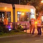 Straßenbahn mit Rollstuhlsymbol an der Tür steht nachts vor Fußgängerfurt, zwei Personen in Warnwesten unter Straßenlaterne. Ein Unfallgutachter an der Straßenbahn.
