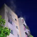 Mehrstöckiges Wohngebäude bei Nacht mit Rauch, der aus einem Fenster aufsteigt.