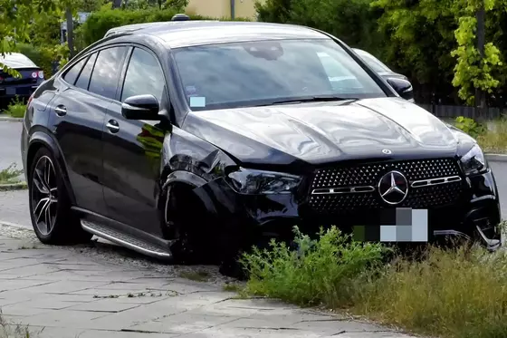Schwarzer Mercedes-Benz SUV mit beschädigtem vorderem linken Kotflügel und fehlendem Vorderrad, geparkt auf einem Gehweg mit Grasbewuchs.