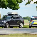 Schwarzer Mercedes SUV mit Dachbox steht auf einer Landstraße, daneben ein Polizeiauto mit Blaulicht und ein Polizist in Uniform.