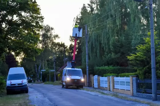 Zwei weiße Transporter stehen auf einer von Bäumen gesäumten Straße, einer mit ausgefahrenem Hebebühnenkorb und einer Person darin.