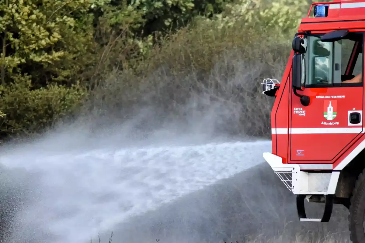 Rotes Feuerwehrfahrzeug sprüht Wasser auf ein abgebranntes Feld.