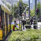 Mehrere Einsatzkräfte der Feuerwehr und Polizei stehen neben einer gelben Straßenbahn an einer Haltestelle in einer städtischen Umgebung.