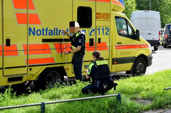 Zwei Polizisten in Uniform neben einem gelb-roten Rettungswagen mit einer Delle.