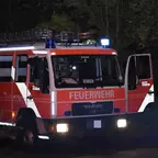 Rotes Feuerwehrfahrzeug mit geöffneten Türen und eingeschaltetem Blaulicht bei Nacht auf einer Straße.