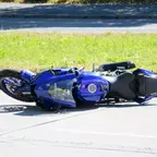 Blaues Motorrad liegt auf der Seite auf einer Straße, im Hintergrund Gras sichtbar.