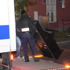 Polizist hebt mit einer weiteren Person einen Spielautomat auf eine LKW-Ladebordwand.